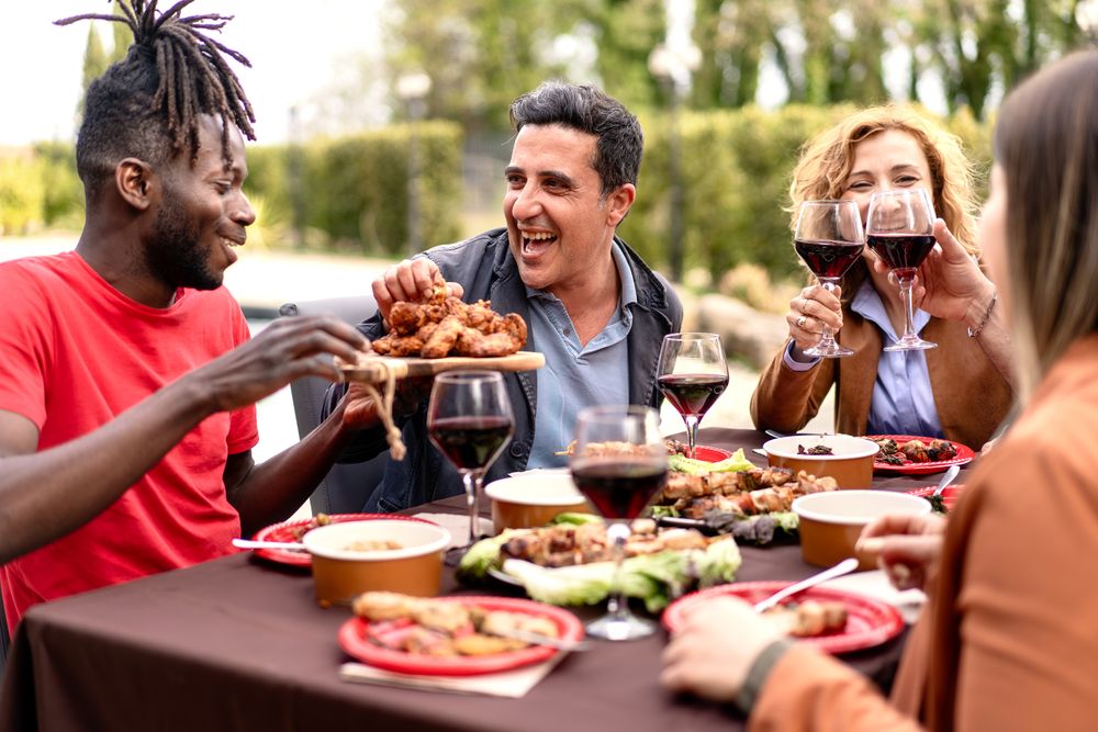 Friends share a laugh over a sumptuous outdoor meal food, toasting with glasses of red wine