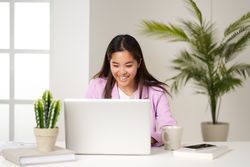 a young asian woman smiling and looking at the computer in the coworking space