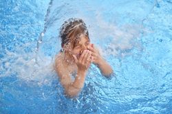 Boy covering nose standing under splashing water in pool