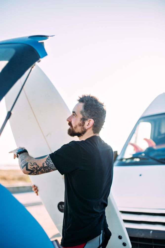 Man loading surfboard into back of vehicle, vertical