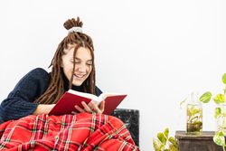 Woman with dreadlocks sitting in a sofa an reading a book