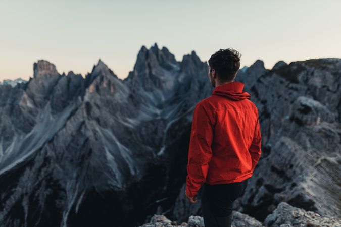 Back view of man in red jacket standing against mountains in Dolomites, Italy