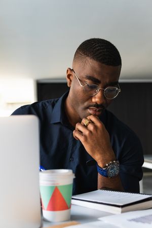 Black man writing in notepad near laptop in office