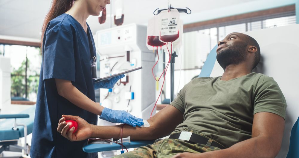 Female Nurse Taking Blood Donation From Black Army Troop In Military Hospital.
