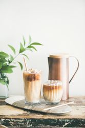 Two glasses of iced coffee and a pitcher, with light background with leaves