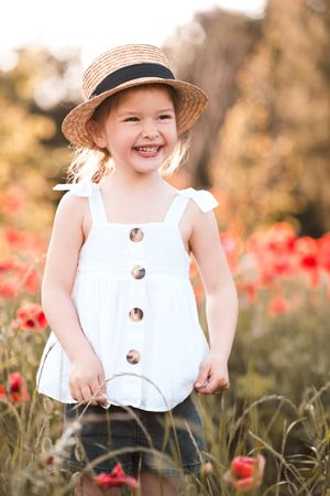 Smiling girl wearing a hat and standing in red flower field