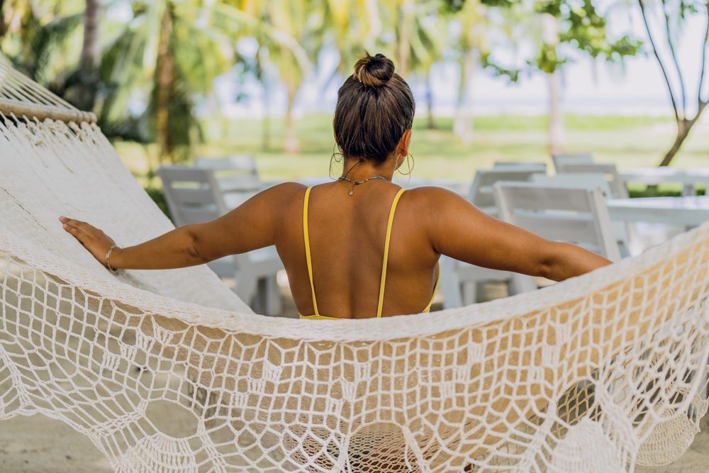 Woman in bikini resting in hummock on beach