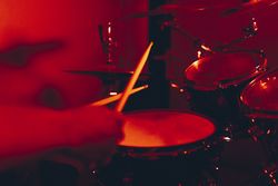 Anonymous man with drumsticks playing on drums in redness