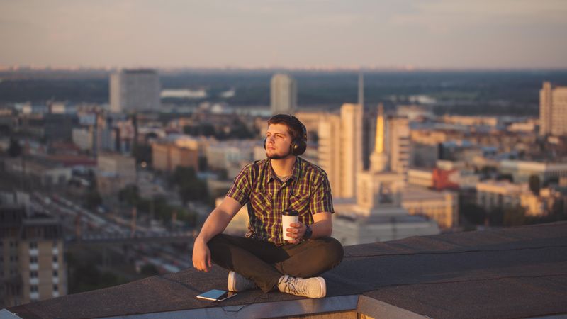 Male with digital tablet and headphones with takeaway coffee cup while enjoying view from rooftop