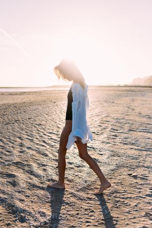 Woman walking on beach with her head down in oversized shirt
