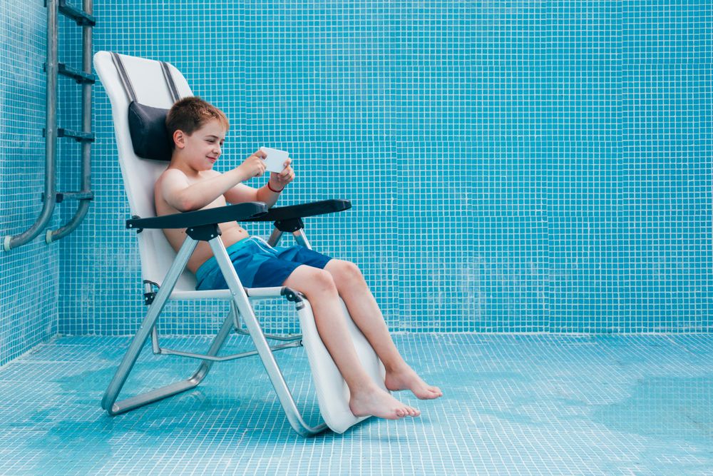 Boy with smartphone sitting on bottom of empty pool