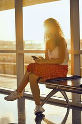 Smiling woman sitting on metal bench with earphones and smartphone