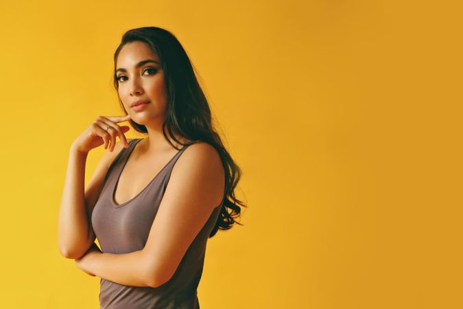 Contemplative Hispanic woman standing and looking at camera in yellow room, copy space