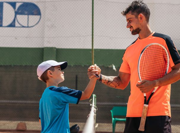 Father and son playing tennis together on a dirt court