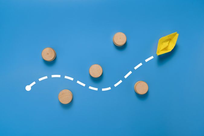 a yellow paper boat passes through barrier. isolated on blue background. concept of avoiding obstacle to achieve a goal