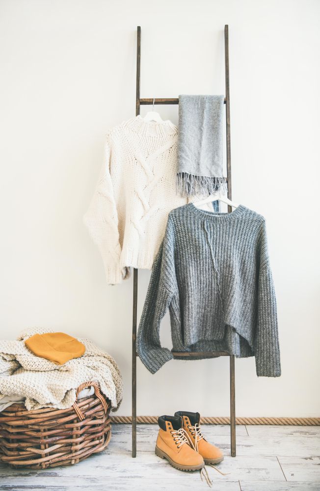 Woolen sweaters, grey scarf, winter boots on modern garment rack, with thatched basket, close up