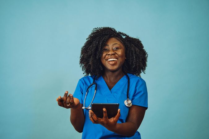 Portrait of happy Black medical professional dressed in scrubs with tablet