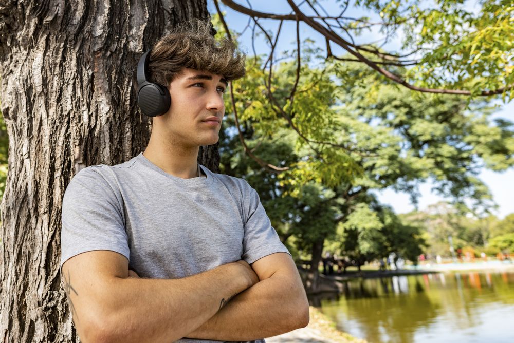 A young man listening to music, leaning on a tree with his arms