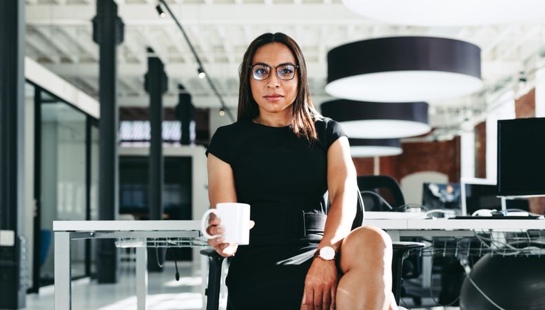 Modern serious businesswoman looking at the camera holding mug