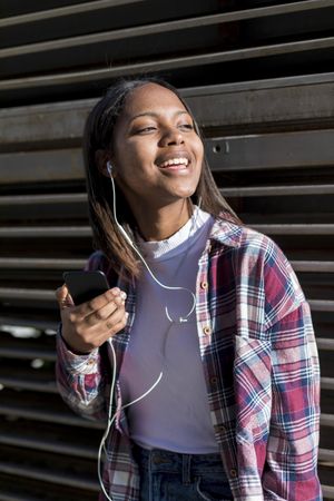 Female leaning on wall outside on sunny day listening to something on smartphone