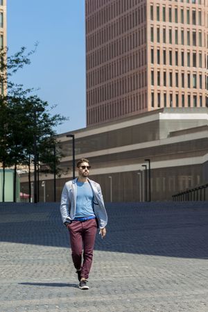 Young bearded man with sunglasses walking on street with hand on pocket looking away