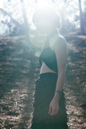 Side view of woman standing in the woods with sun flare