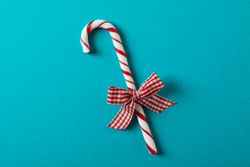 Sweet candy cane with bow on turquoise background, space for text