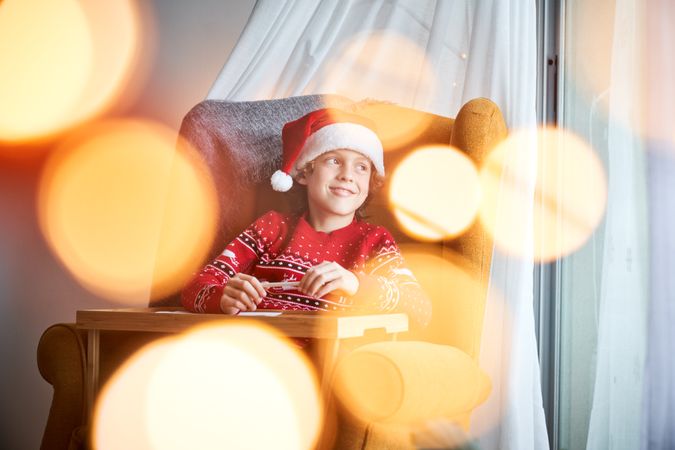 Child with pencil dreaming in armchair near table in Christmas