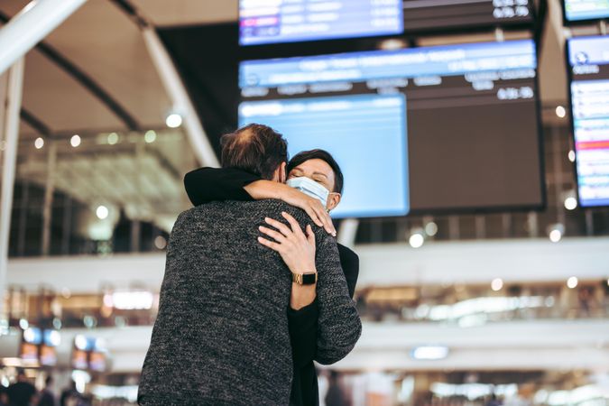 Female in face mask hugging her husband at airport