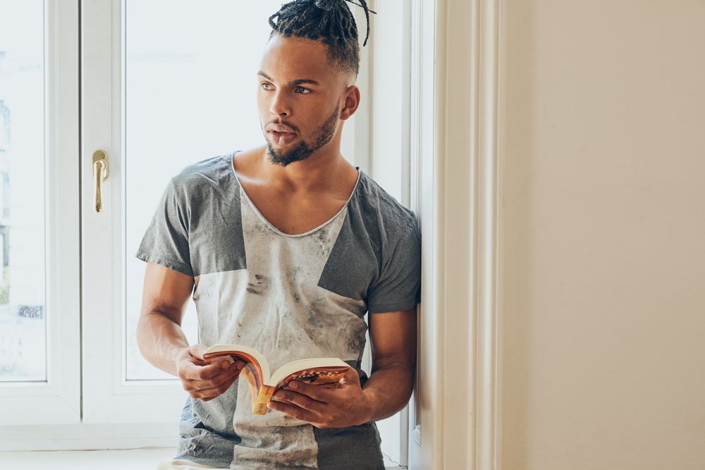 Black male standing by window and reading
