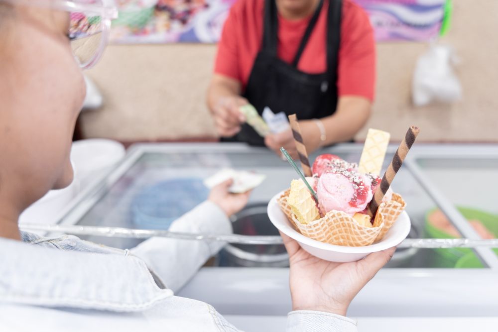 A young Hispanic woman is waiting for her change while holding a big traditional Mexican ice cream