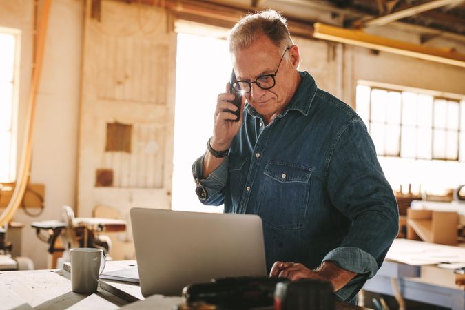 Older man talking on cell phone and using laptop on work table