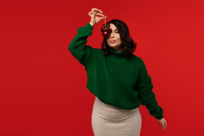 Woman holding red Christmas bauble near her face.