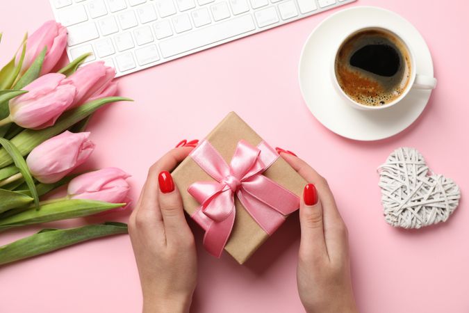 Young woman hold gift on decorated pink background, top view