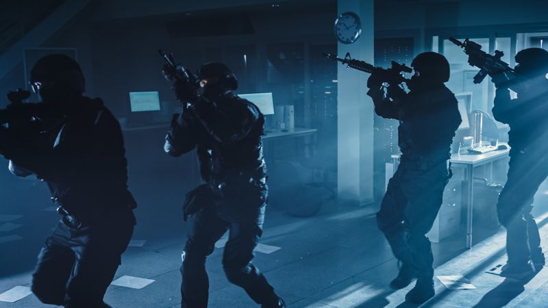 Masked Squad of Armed SWAT Police Officers Move in a Hall of a Dark Seized Office Building with Desks and Computers.