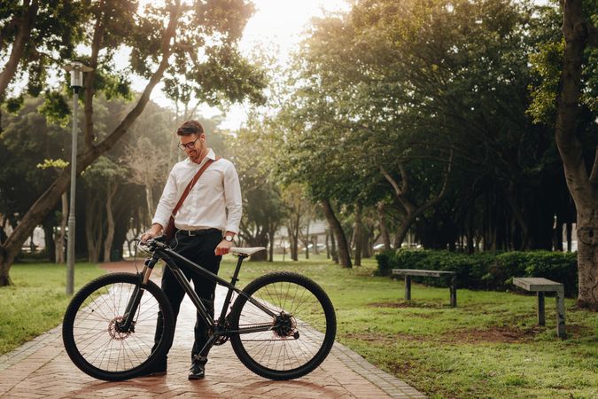 Smiling businessman looking at his bike standing in the park