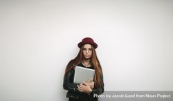 Stylish woman holding laptop standing against a light wall 5QnJd4