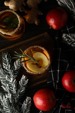 Glasses with apple cider, branches of christmas tree and apples on dark wooden background, top view