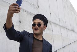 Young Latino gay man with make-up on wearing a fashionable hat and sunglasses, taking selfies