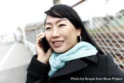 East Asian woman in red scarf and dark jacket having a phone call outdoor 5XJPQb