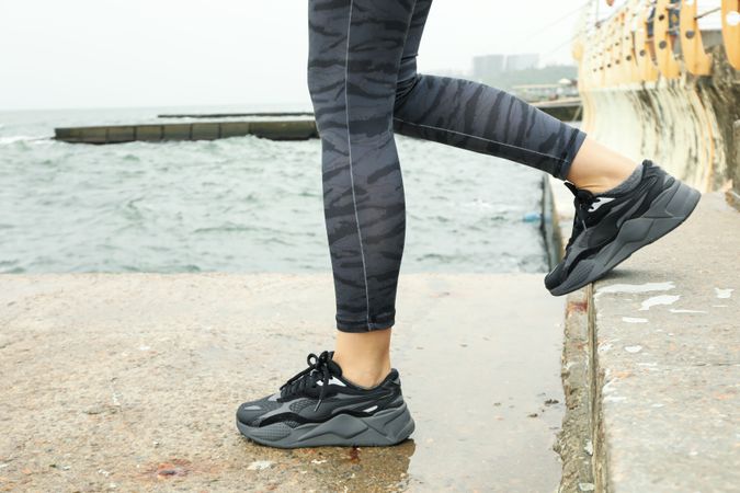 Female legs in leggings and sneakers on the sea pier