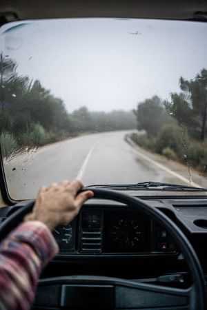 Driver riding car along rural pathway at forest in rain