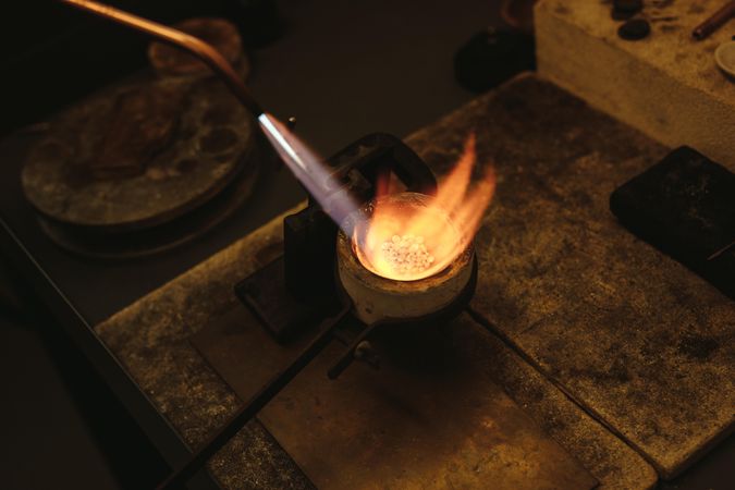 Goldsmith using torch flame to heat and melt the silver granules in a crucible