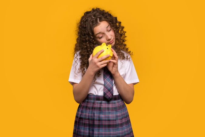 Girl holding piggy bank close, school uniform.
