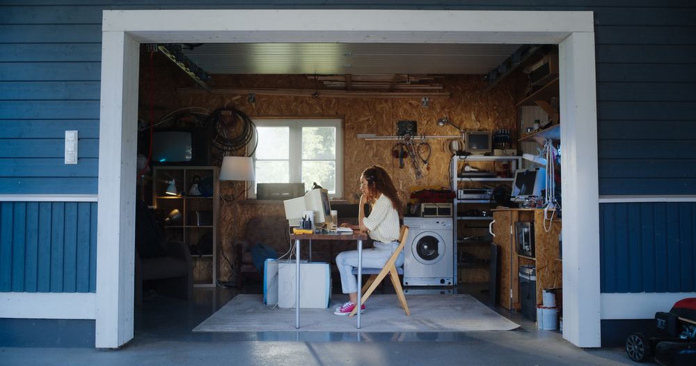 Hispanic Female Developer Programming On Old Desktop Computer In Retro Garage With Random Appliances.