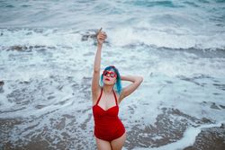 Cheerful stylish woman raising hands in foamy ocean water