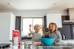Young girl licking batter from spatula with her brother holding a whisk bezkq0