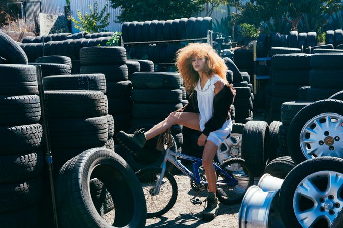Young woman with afro sitting outside on bike at tire shop