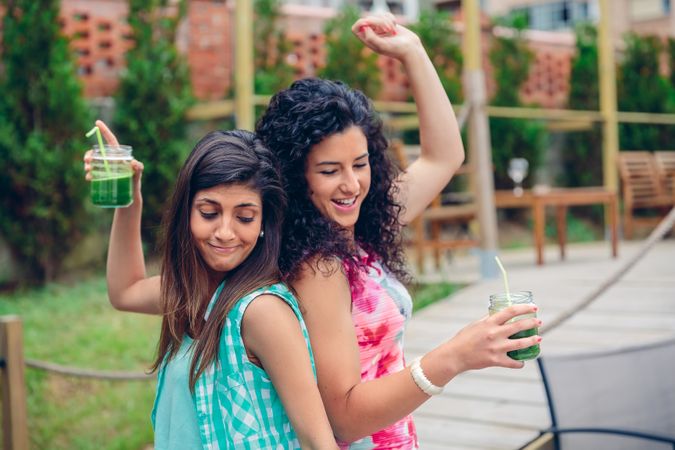 Two female friends dancing outside with cocktails