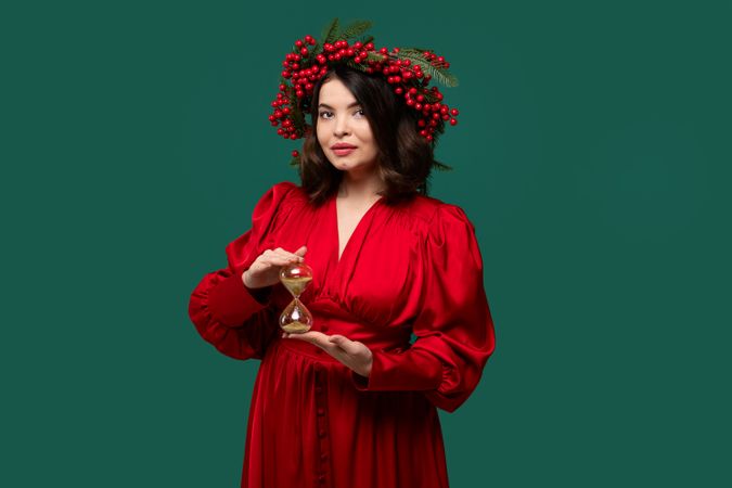 Stylish woman with berry wreath stopping hourglass sand flow.